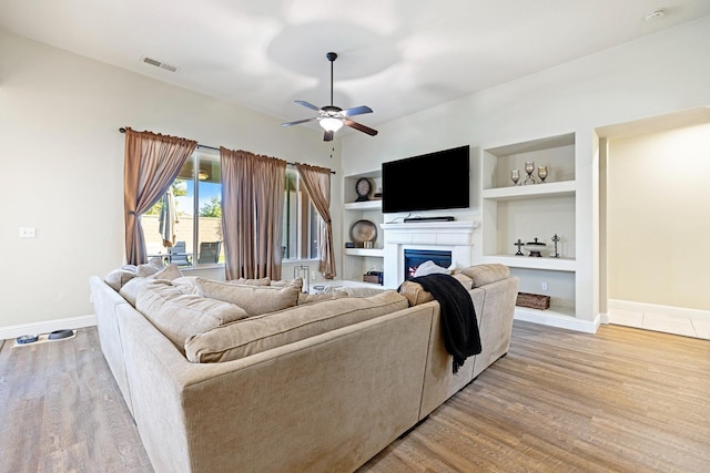 living room featuring built in features, light wood-type flooring, and ceiling fan