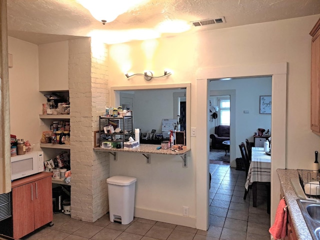 kitchen featuring a breakfast bar area, sink, light tile patterned flooring, and a textured ceiling