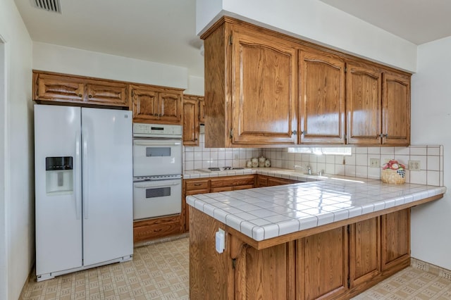 kitchen featuring decorative backsplash, tile countertops, kitchen peninsula, sink, and white appliances