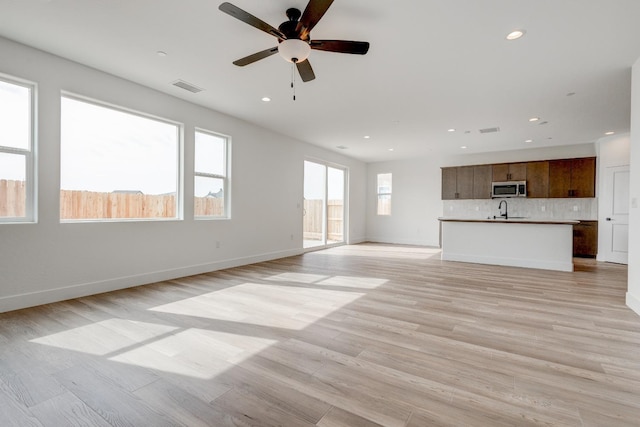 unfurnished living room featuring sink, ceiling fan, and light hardwood / wood-style flooring