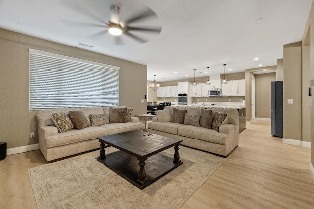 living room featuring sink, ceiling fan with notable chandelier, and light wood-type flooring