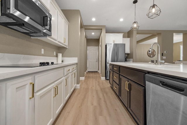 kitchen with white cabinets, appliances with stainless steel finishes, light wood-type flooring, sink, and decorative light fixtures