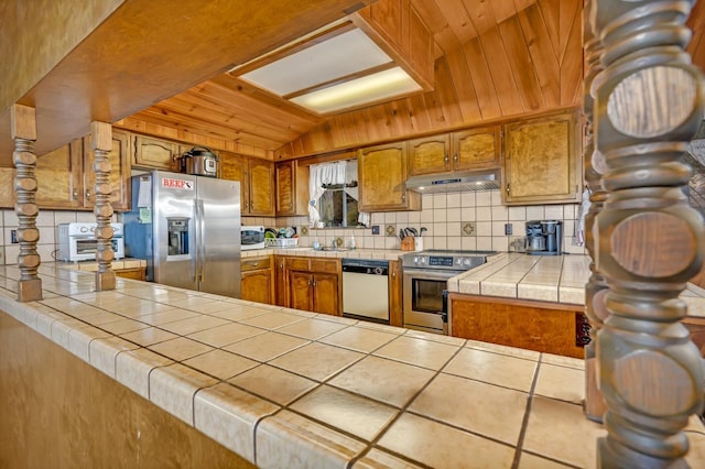 kitchen featuring appliances with stainless steel finishes, tile counters, lofted ceiling, and kitchen peninsula