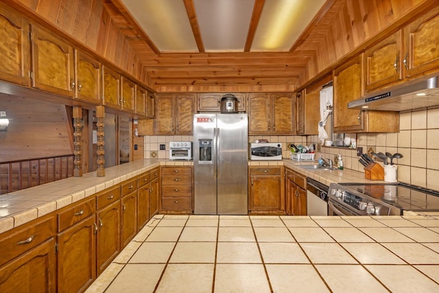 kitchen with tasteful backsplash, appliances with stainless steel finishes, light tile patterned flooring, tile countertops, and wooden walls