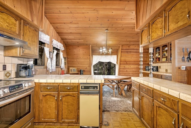 kitchen with tile countertops, an inviting chandelier, wooden walls, and stainless steel electric range oven