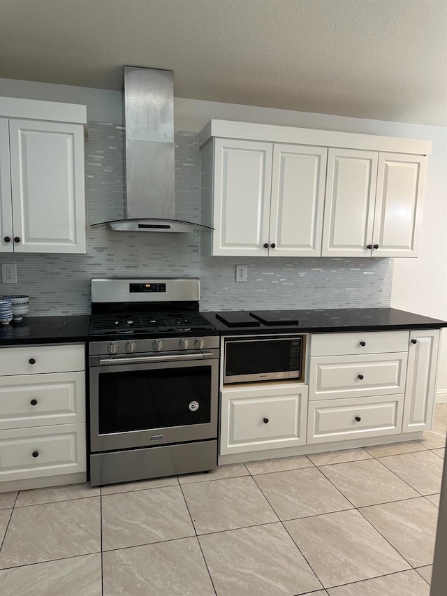 kitchen with white cabinets, wall chimney range hood, built in microwave, stainless steel gas stove, and dark countertops