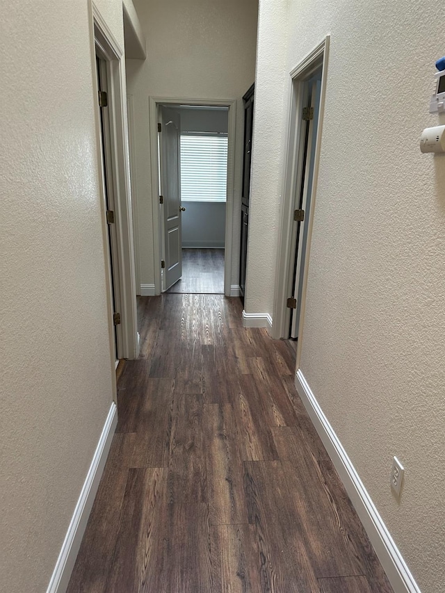 hallway featuring baseboards, dark wood-type flooring, and a textured wall