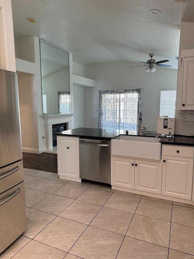 kitchen with a glass covered fireplace, stainless steel appliances, white cabinetry, a sink, and light tile patterned flooring