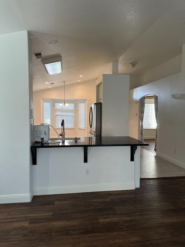 kitchen featuring dark countertops, wood finished floors, freestanding refrigerator, vaulted ceiling, and a sink