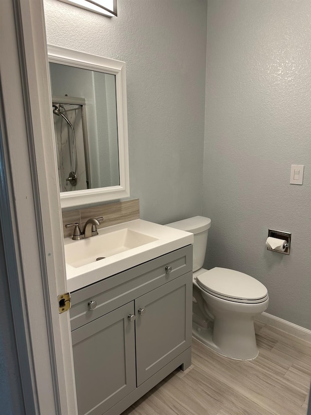 bathroom featuring a textured wall, vanity, toilet, and baseboards