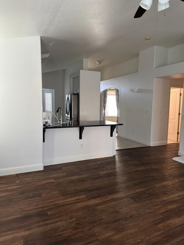 unfurnished living room featuring a textured ceiling, a sink, wood finished floors, a ceiling fan, and baseboards