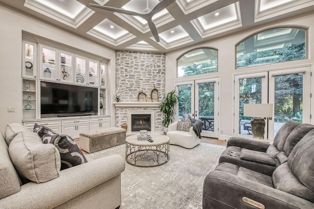 living room with a towering ceiling, french doors, a stone fireplace, coffered ceiling, and beam ceiling