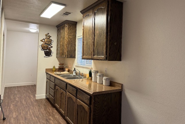 bar featuring sink, dark brown cabinetry, dark hardwood / wood-style floors, and a textured ceiling