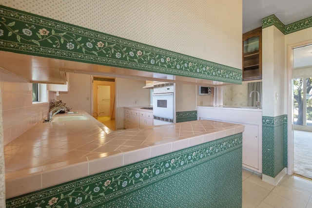 kitchen with white oven, sink, gas stovetop, and tile counters