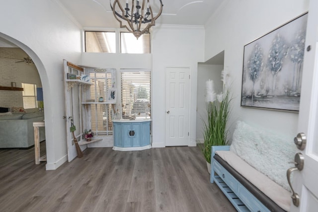 entryway with a towering ceiling, ornamental molding, dark wood-type flooring, and ceiling fan with notable chandelier