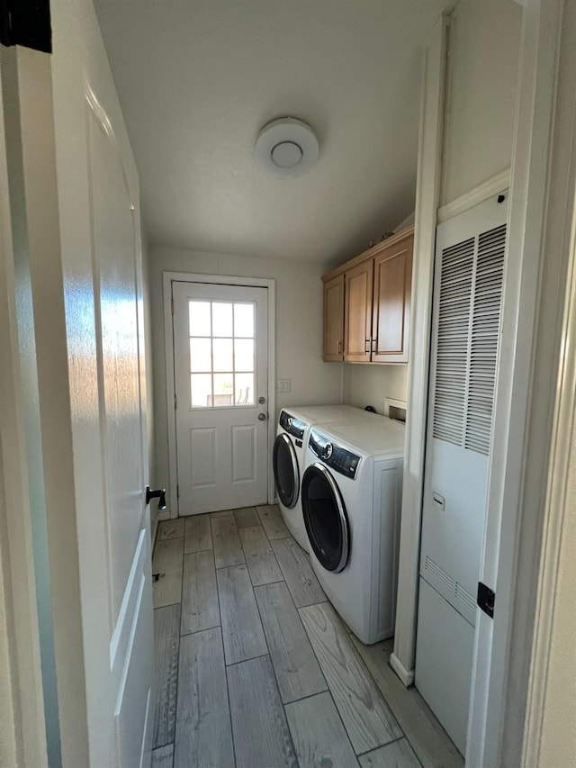 laundry area featuring washing machine and clothes dryer, light wood-type flooring, and cabinets