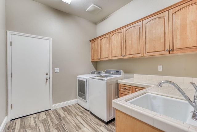 laundry area with cabinets, sink, washing machine and clothes dryer, and light wood-type flooring