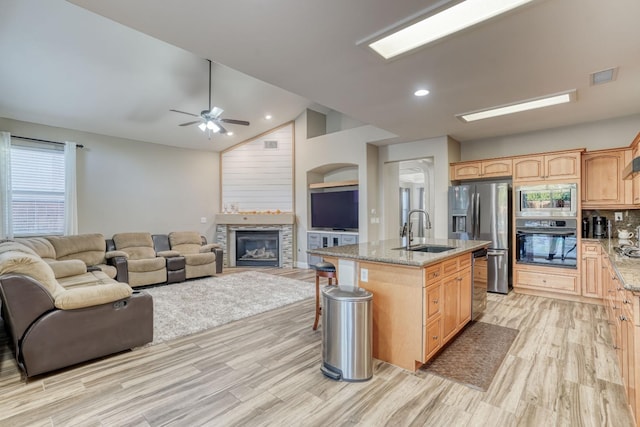 kitchen featuring stainless steel appliances, a center island with sink, sink, light wood-type flooring, and light stone counters