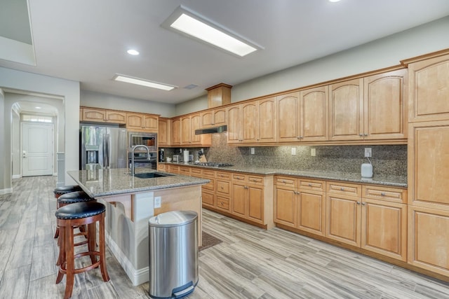 kitchen with tasteful backsplash, an island with sink, appliances with stainless steel finishes, light wood-type flooring, and sink