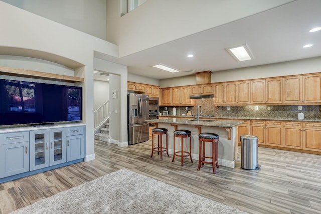 kitchen featuring an island with sink, light hardwood / wood-style floors, stainless steel appliances, decorative backsplash, and a breakfast bar area