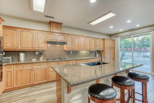 kitchen with sink, a kitchen island with sink, decorative backsplash, and light wood-type flooring