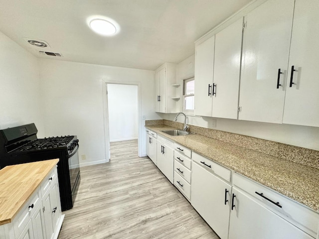 kitchen with white cabinets, sink, black gas range oven, and light wood-type flooring