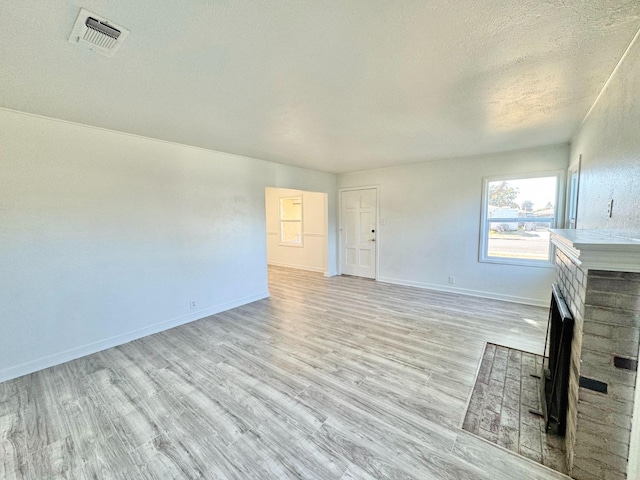 unfurnished living room with a fireplace, a textured ceiling, and light wood-type flooring