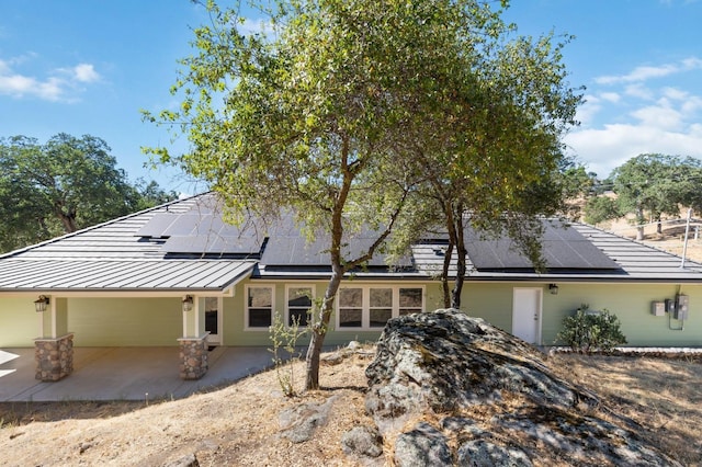 view of front of home featuring a standing seam roof, a patio area, metal roof, and solar panels