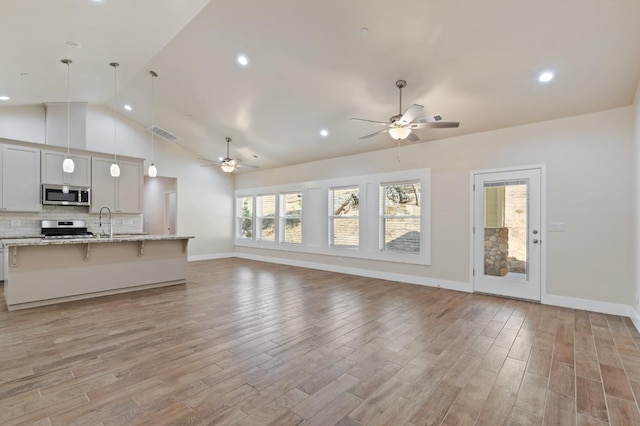 unfurnished living room with ceiling fan, a sink, visible vents, baseboards, and light wood finished floors