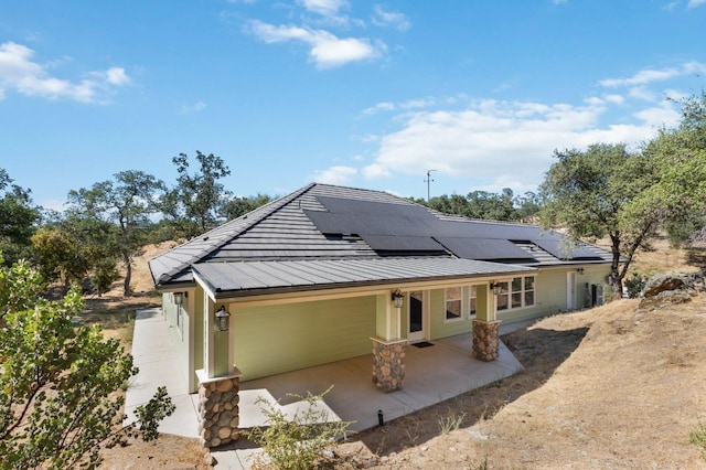 view of front of house featuring a standing seam roof, roof mounted solar panels, metal roof, and a patio