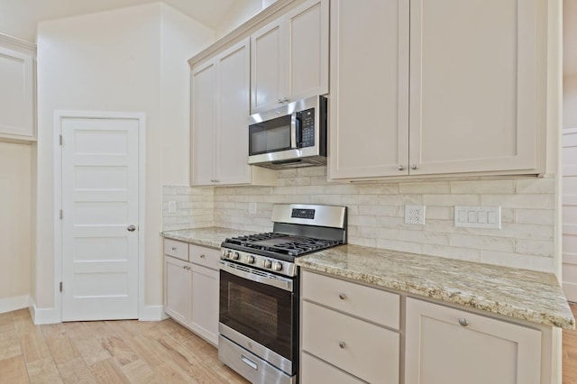 kitchen with stainless steel appliances, white cabinetry, backsplash, and light stone counters