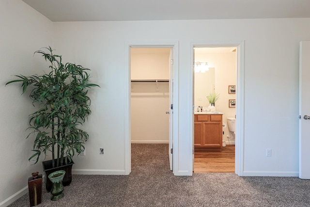 bedroom with connected bathroom, a walk in closet, a closet, and dark carpet