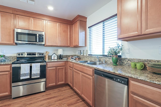 kitchen with appliances with stainless steel finishes, light hardwood / wood-style floors, light stone counters, and sink