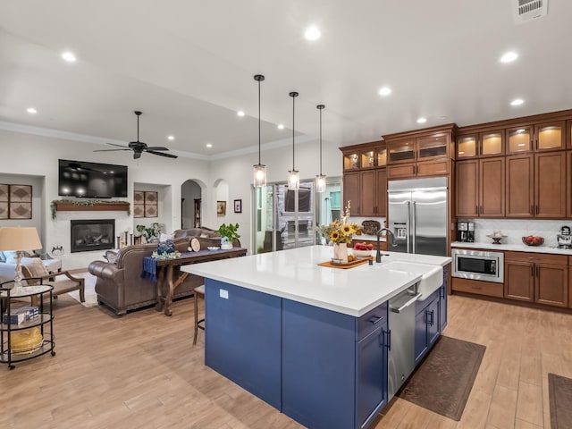 kitchen featuring sink, hanging light fixtures, built in appliances, ceiling fan, and an island with sink