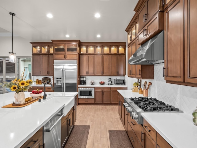 kitchen featuring sink, wall chimney exhaust hood, tasteful backsplash, built in appliances, and decorative light fixtures