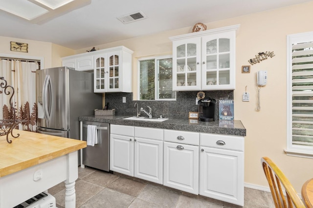 kitchen with light tile patterned floors, backsplash, white cabinetry, sink, and stainless steel appliances