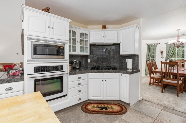 kitchen featuring stainless steel appliances, backsplash, light tile patterned flooring, a notable chandelier, and white cabinetry