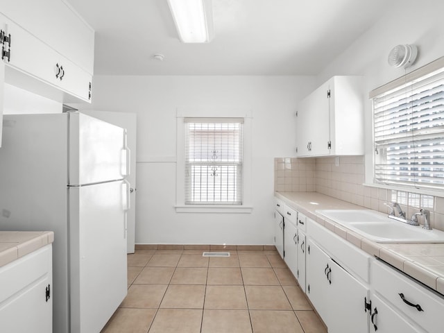 kitchen with tasteful backsplash, sink, tile counters, white cabinets, and white refrigerator