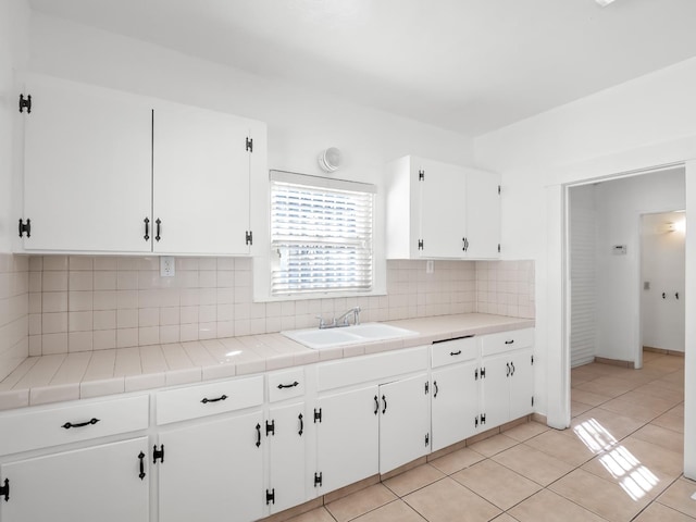 kitchen with tile countertops, sink, white cabinets, and backsplash