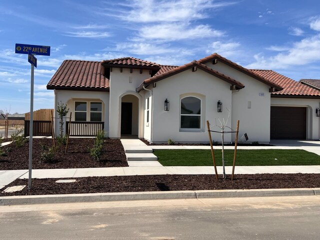 mediterranean / spanish house with driveway, a tile roof, an attached garage, fence, and stucco siding