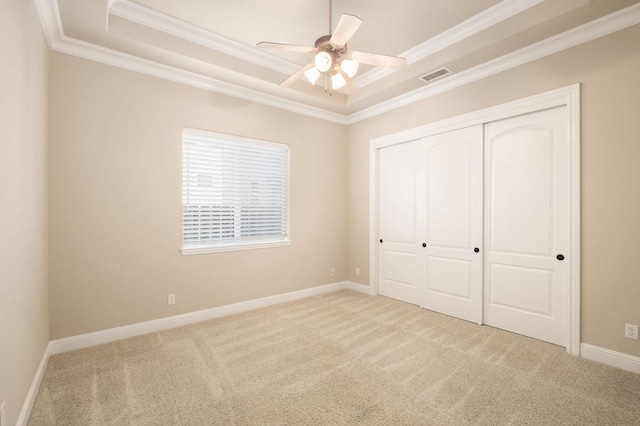 unfurnished bedroom with crown molding, ceiling fan, light colored carpet, and a raised ceiling