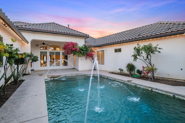 pool at dusk with french doors, a patio area, pool water feature, and ceiling fan