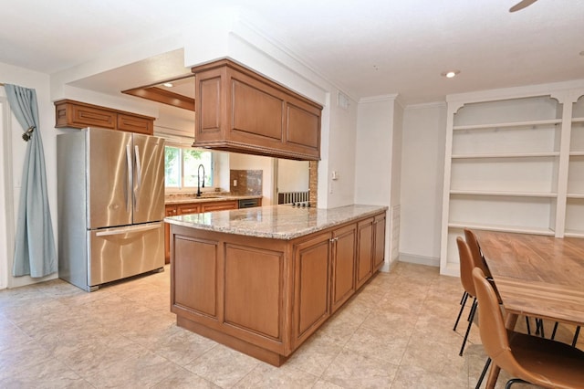 kitchen with light stone counters, brown cabinets, a sink, and freestanding refrigerator