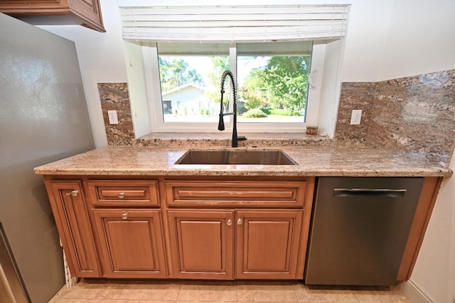 kitchen with light stone counters, brown cabinetry, a sink, and stainless steel dishwasher