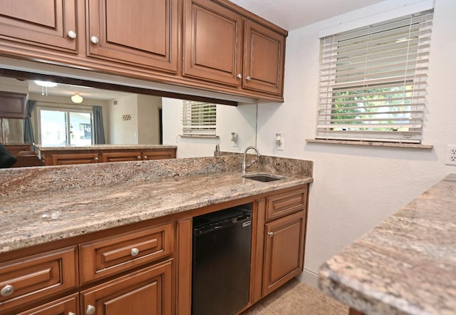 kitchen with black dishwasher, brown cabinets, a sink, and light stone countertops