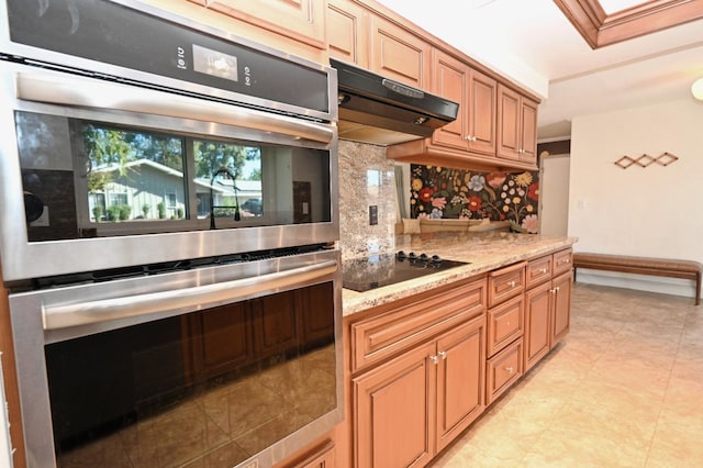 kitchen with stainless steel double oven, black electric cooktop, under cabinet range hood, light stone countertops, and tasteful backsplash