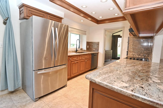 kitchen featuring light stone counters, stainless steel appliances, a sink, tasteful backsplash, and brown cabinetry