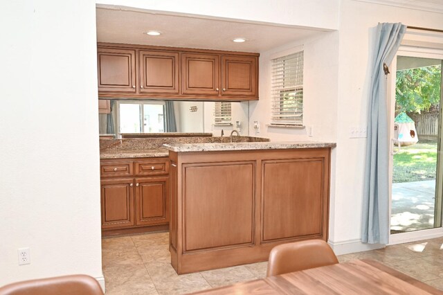 kitchen with light stone countertops, recessed lighting, brown cabinetry, and light tile patterned flooring