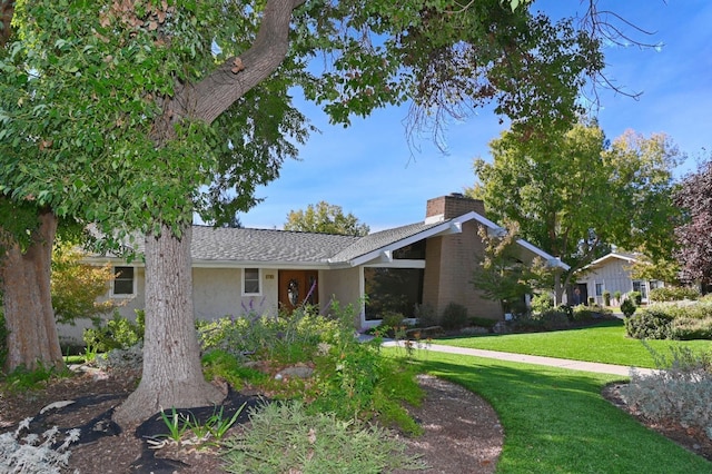 view of front facade with roof with shingles, a front lawn, a chimney, and stucco siding