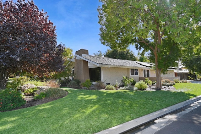 view of front facade featuring a front yard, stucco siding, a chimney, and solar panels